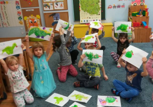 Dzieci siedzą na dywanie prezentują rysunki smoków.